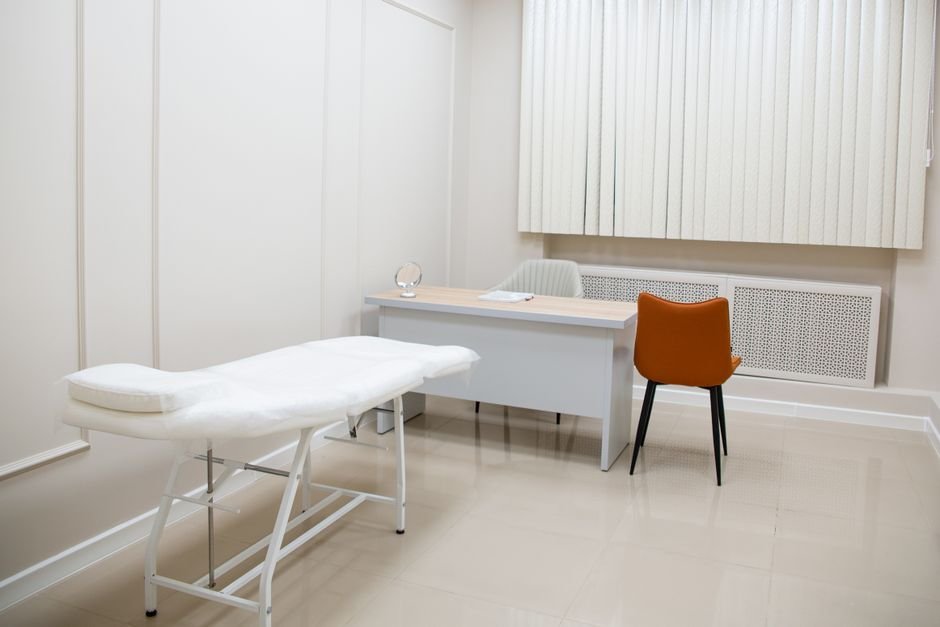Masası, sandalyeleri ve muayene yatağı olan minimalist muayene odası